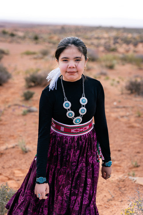 A young native teenager wearing traditional regalia outside