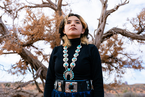 A young native teenager wearing traditional regalia outside