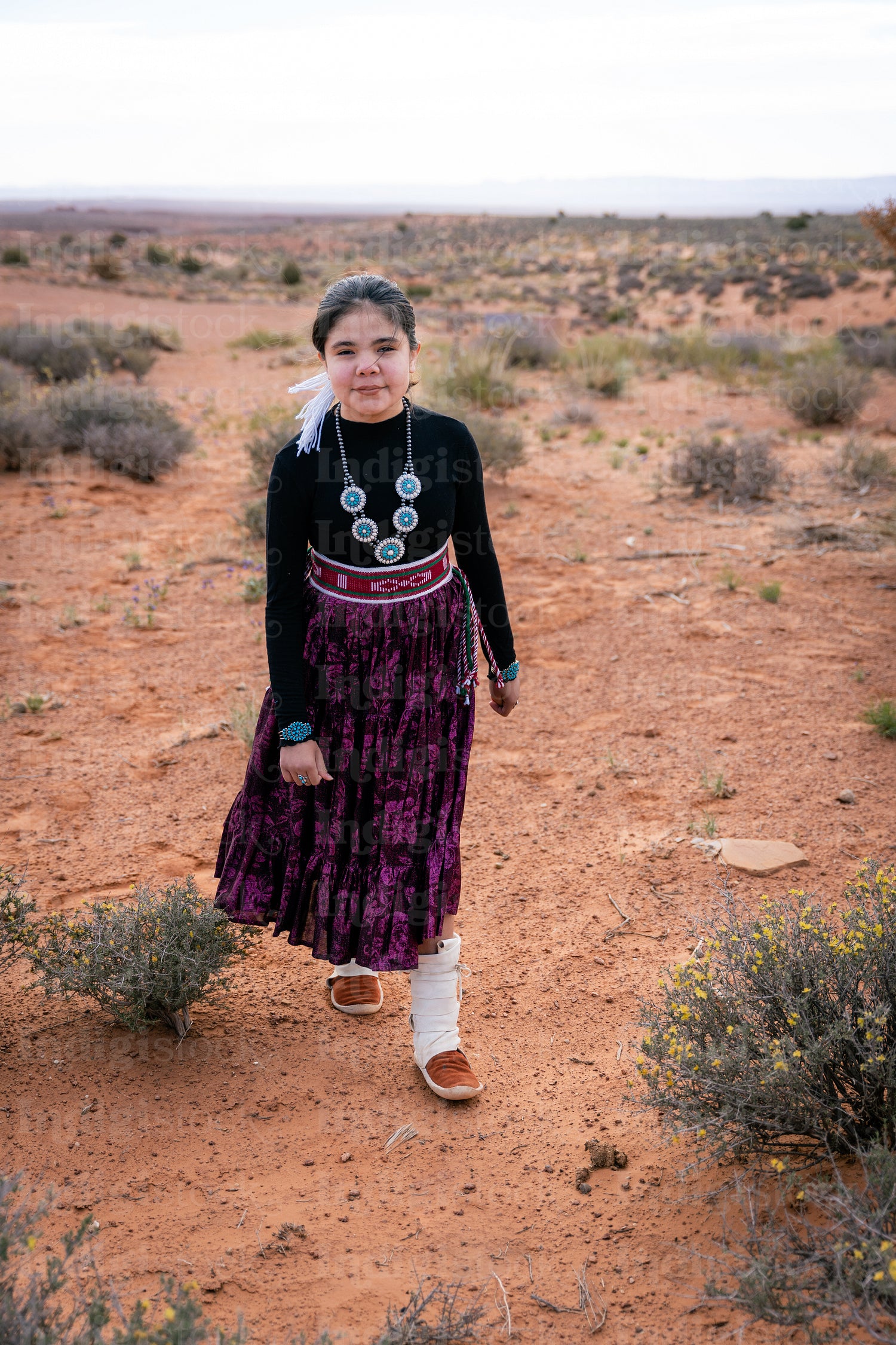 A young native teenager wearing traditional regalia outside