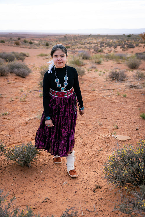 A young native teenager wearing traditional regalia outside