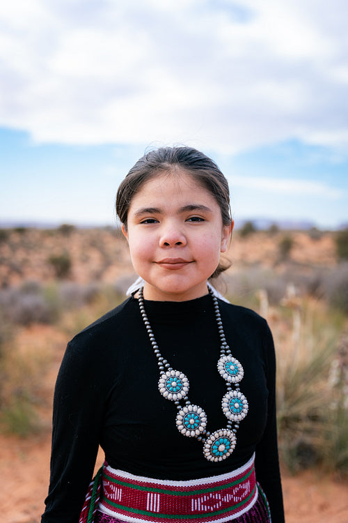 A young native teenager wearing traditional regalia outside