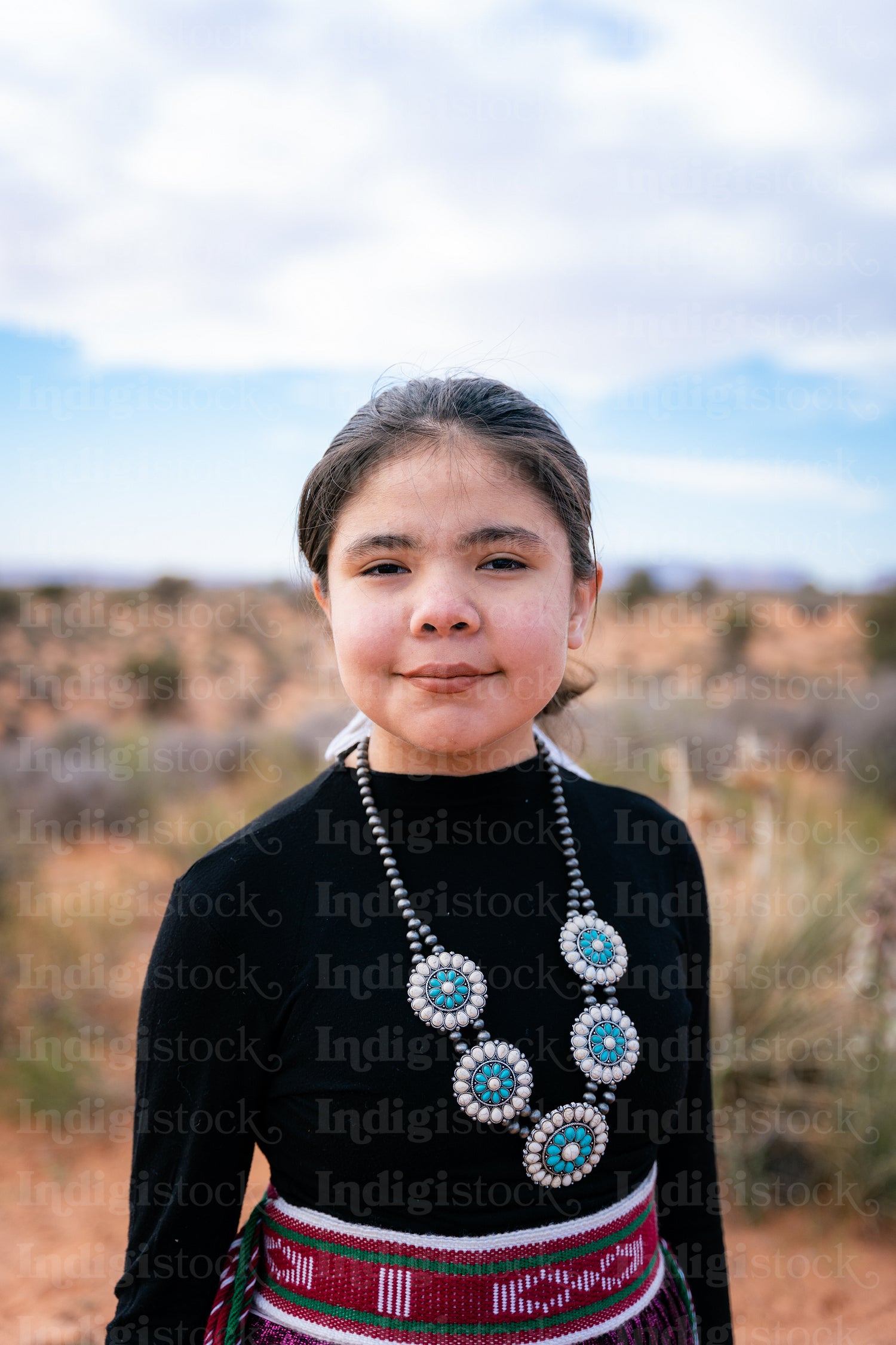 A young native teenager wearing traditional regalia outside